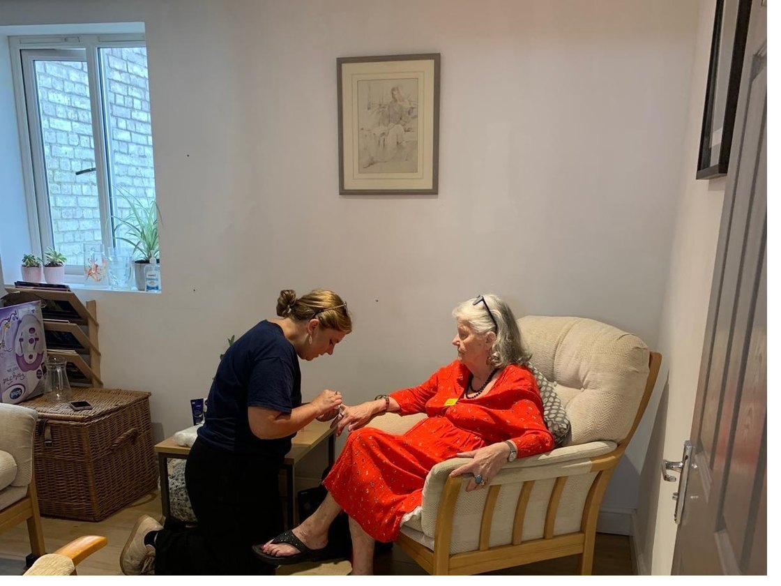A carer sitting beside a lady in her own front room, chatting over a cup of tea