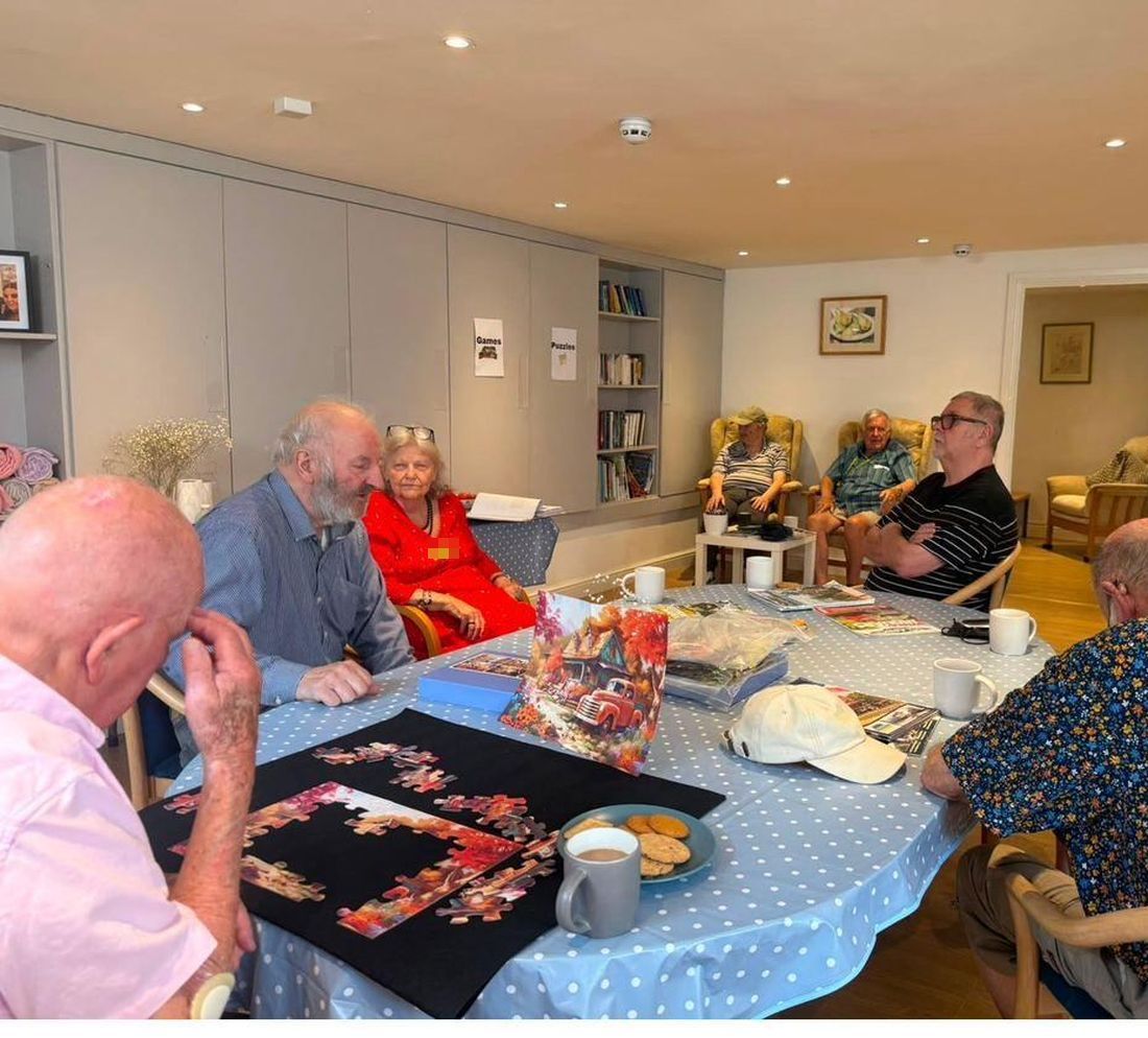 A group working on a jigsaw together over mugs of tea and a plate of biscuits
